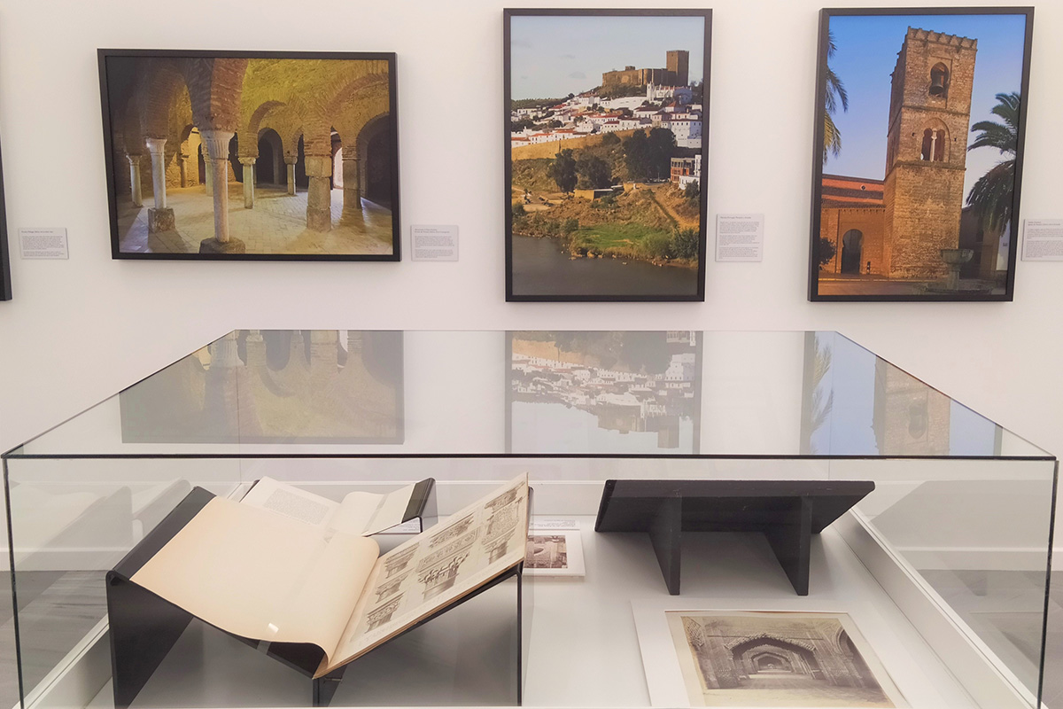 Showcase containing different exhibits on the architecture of al-Andalus, dating from the 19th century. In the background wall, pictures showing buildings of al-Andalus to be found in Almonaster la Real, Mértola and Niebla.